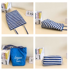 Detail view of striped canvas tote bag showing stitching and 'merci' print on fabric