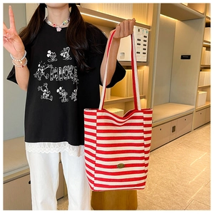Detail of red and white striped canvas tote bag showing the metal logo and long handles