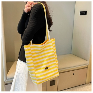 Detailed side view of yellow and white striped canvas tote bag worn by a model