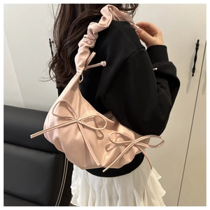 Close-up of pink bow shoulder bag with ruffled straps shown on model's shoulder