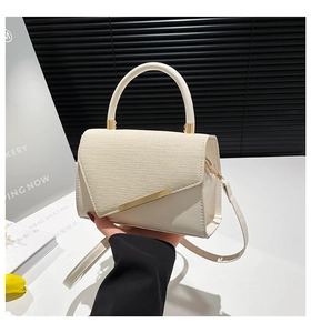 Detail of cream leather handbag with woven texture flap and golden metal bar accessory