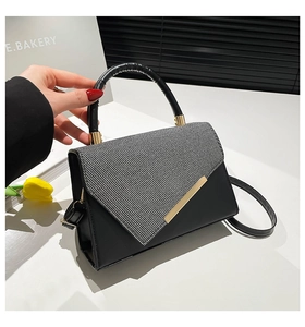 Detail of minimalist black crossbody bag with gold buckle and stylish circular handle