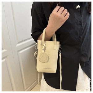 Close-up of cream vertical bucket bag with cute dog charm and slim shoulder strap