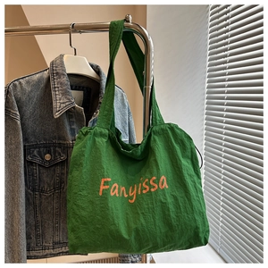 Detail of green canvas tote bag with orange lettering hanging next to a denim jacket