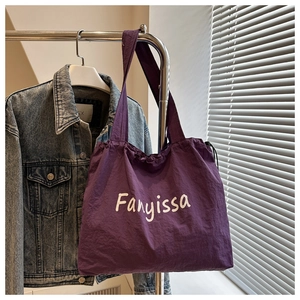 Detail of purple nylon tote bag with white Fanyissa script and drawstring closure