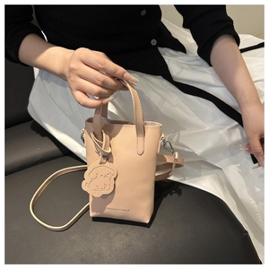 Detail of beige mini crossbody bag with a cute dog pendant and metal buckle strap