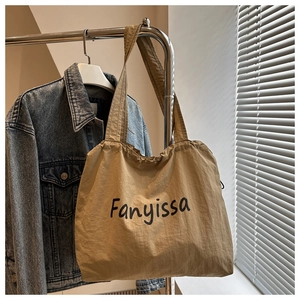 Detail of khaki nylon tote bag with black Fanyissa logo hanging in a casual setting