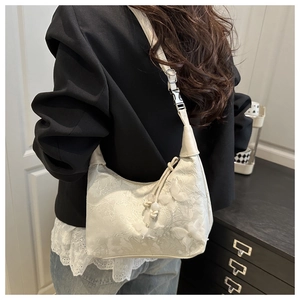 Detail of white lace hobo bag featuring 3D butterfly accents and woven tassel charms