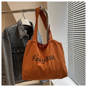 Detail of orange drawstring tote bag with black Fanyissa logo on a metal hanger