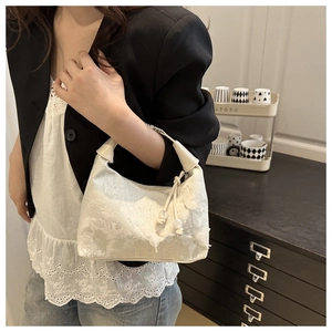 Detail of white lace handbag featuring floral textures, tassels, and pearl pendant accents