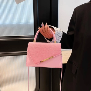 Pink crossbody bag with woven flap and gold metal trim shown in model hand