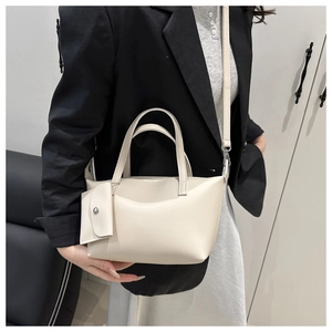 Minimalist cream leather bucket bag shown on model with shoulder strap and small pouch