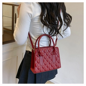 Side view of a red quilted leather tote bag worn by a model in a minimalist urban setting