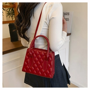 Detail of red quilted faux leather handbag with diamond pattern and rolled top handles