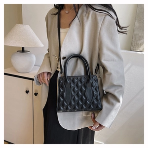 Close-up of a black quilted tote bag with diamond stitching held by a model