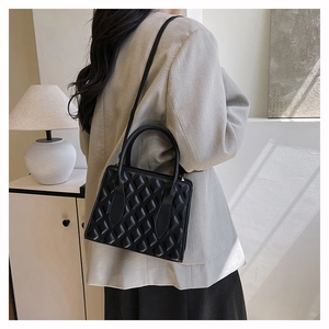 Detail of black quilted leather crossbody bag featuring classic diamond stitching pattern