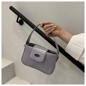 Close-up of lavender glossy patent leather handbag with silver oval brand plaque