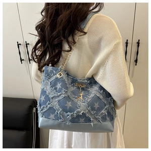 Detail of blue denim tote bag with star print, gold chain strap, and deer charm detail