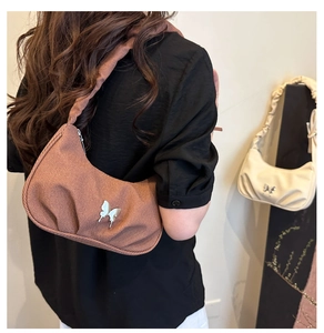 Détail d'un sac à épaule plissé rouge rouille avec un charmant papillon en métal doré
