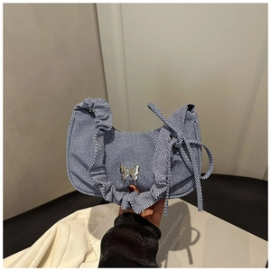 Gros plan du sac hobo en denim bleu avec papillon en métal argenté et détails plissés