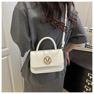 Détail d'un sac blanc tissé avec logo M doré et bandoulière réglable pour femmes