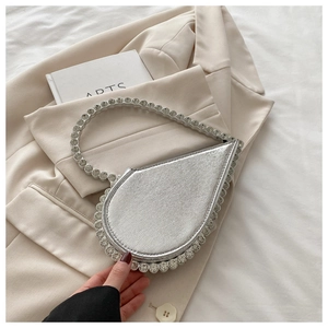 Close-up of heart-shaped silver handbag with sparkling crystals on beige suit background