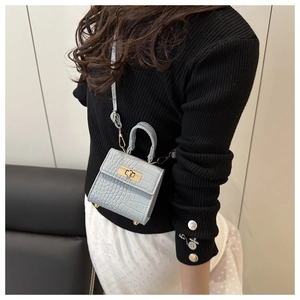 Detail of light blue croc-embossed micro bag with gold twist lock on black sweater