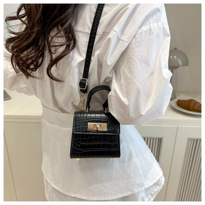 Detail showing mini black crocodile embossed crossbody bag with gold hardware on model