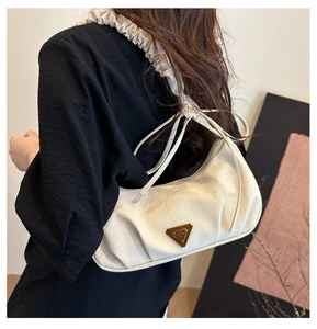 Detail of cream pleated shoulder strap and metallic triangular plaque on hobo bag