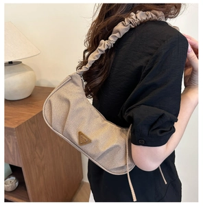 Close-up of beige ruched shoulder bag with gold triangular logo on pleated fabric