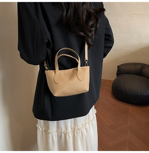 Model wearing a beige lychee leather mini tote bag with gold hardware and shoulder strap