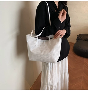 Detailed close-up of a white woven tote bag showing texture and leather patch detail