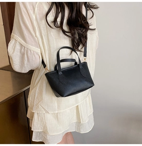 Detail of black lychee grain leather tote bag with gold metal clasp on white dress