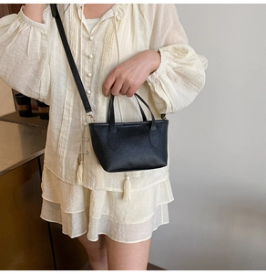 Close-up of black lychee grain leather handbag with gold hardware on white blouse