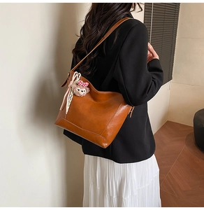 Detail of a brown leather hobo bag featuring an elegant silk scarf and plush charm accessory