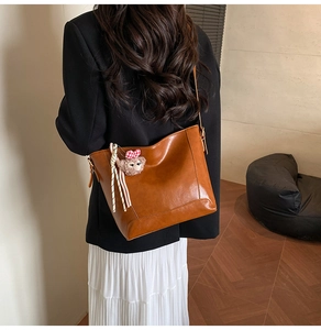 Close-up of brown leather bucket bag with cute plush bear charm on the side