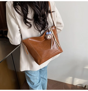 Detail view of brown leather bucket tote bag with decorative striped rope and plush charm