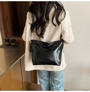 Glossy black leather bucket bag worn by model in a minimalist stylish outfit