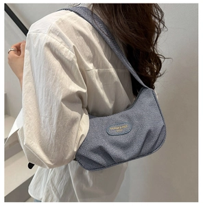 Dettaglio borsa a spalla in denim a righe blu con cerniera metallica e logo ovale