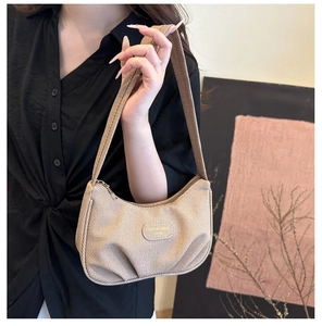 Dettaglio borsa hobo beige a pieghe con logo dorato su modella con camicia nera