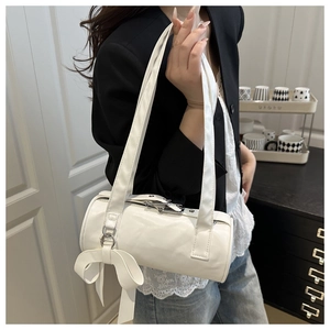 Detail of white cylinder bag featuring a large decorative bow and wide shoulder straps