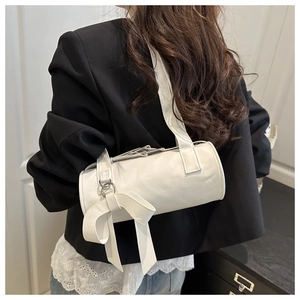 White cylinder shoulder bag featuring elegant side ribbon bow and wide strap on model
