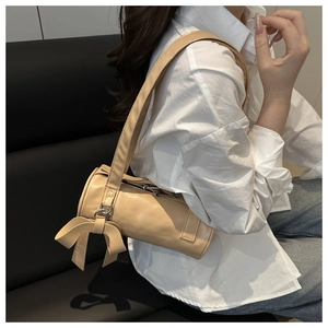 Detail of beige cylindrical baguette bag featuring a stylish side ribbon bow decoration