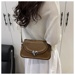 Détail d'un sac besace en cuir marron foncé avec boucle coeur argentée sur un modèle