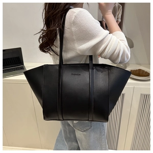 Detail of matte black leather tote bag with FASHION embossed logo and slender straps