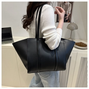 Detailed side view of a large black matte tote bag worn by a model in a modern room