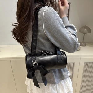 Minimalist black cylinder shoulder bag with a silk bow shown from a stylish side angle
