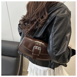 Detail of a dark brown vintage saddle bag with metal buckle worn over the shoulder