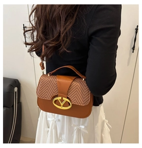 Detalle de bolso de cuero marrón con solapa de tejido de espiga y hebilla de metal en V