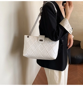Detail of white quilted faux leather bag featuring a twist lock and metal chain strap